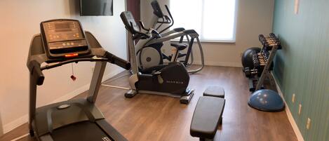 A gym with a treadmill, elliptical, stationary bike, and free weights.