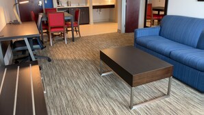 A modern living room with a blue sofa, a wooden coffee table, and a dining area with red chairs. - Holiday Inn Express & Suites Exmore - Eastern Shore by IHG (Exmore)