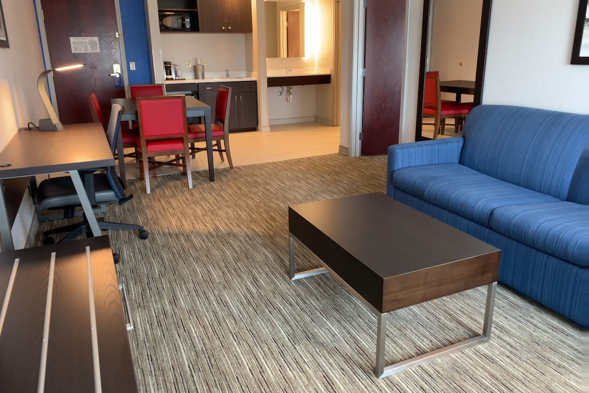A modern living room with a blue sofa, a wooden coffee table, and a dining area with red chairs.