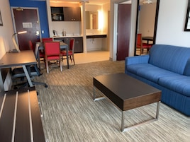 Una sala moderna con un sofá azul, una mesa de centro de madera y un comedor con sillas rojas.