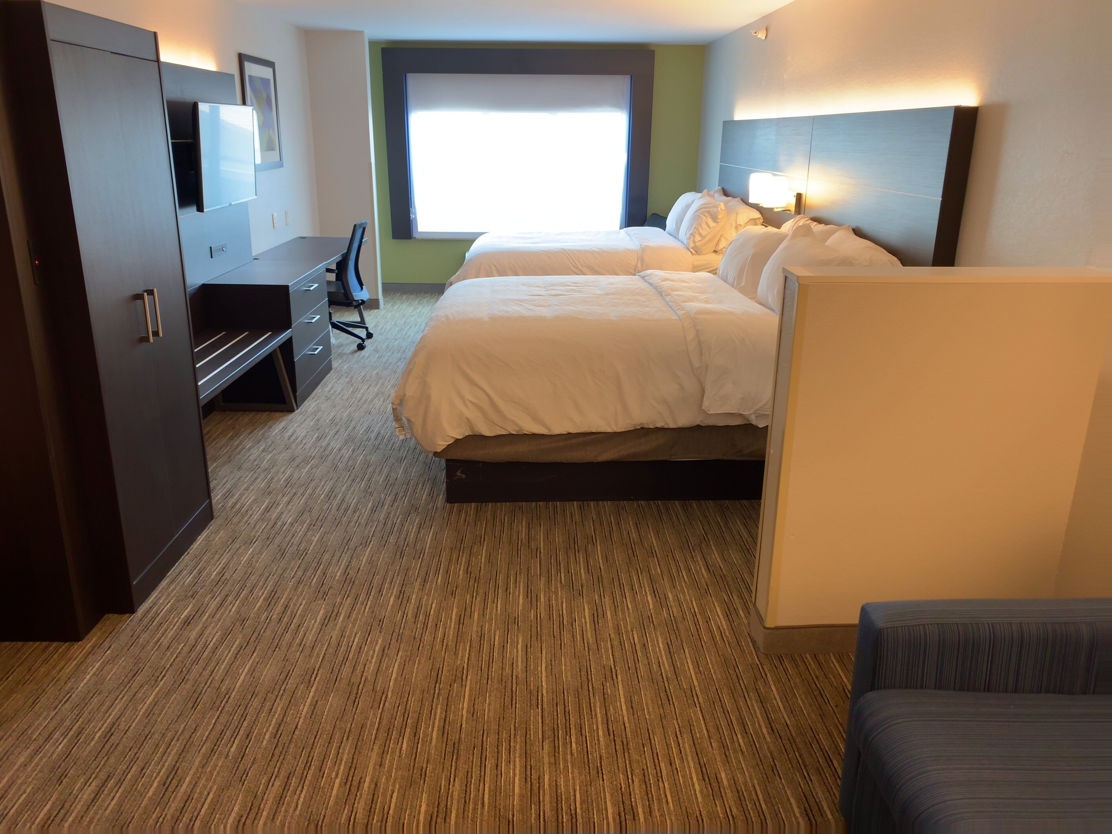 A hotel room with a bed, a desk, a chair, and a TV.