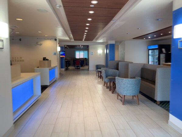 A modern hotel lobby with a reception desk, seating area, and a counter with a beverage dispenser. - Holiday Inn Express & Suites Exmore - Eastern Shore by IHG (Exmore)