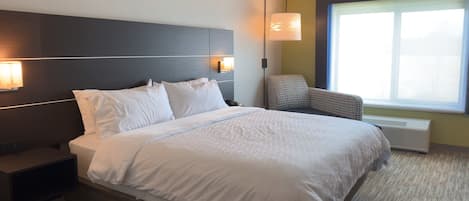 A modern hotel room with a large bed, bedside lamps, a chair, and a large window.