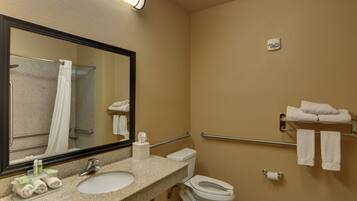 A bathroom with a sink, toilet, and a mirror. There are towels on a rack and a fire extinguisher on the wall.