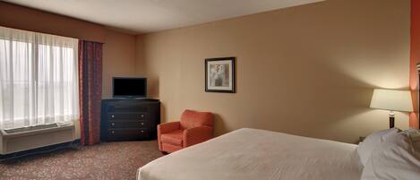 A hotel room with a bed, a dresser, a television, a chair, and a picture on the wall.