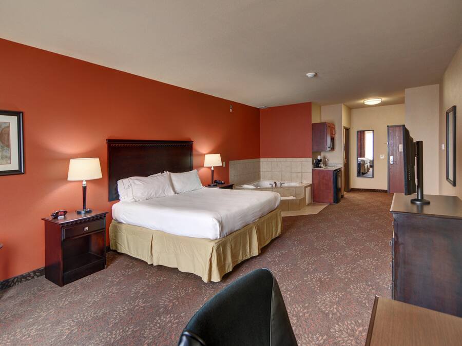 Habitación de hotel con una cama grande, dos mesitas de noche con lámparas, un escritorio, una silla, televisión y un baño con bañera y lavabo.
