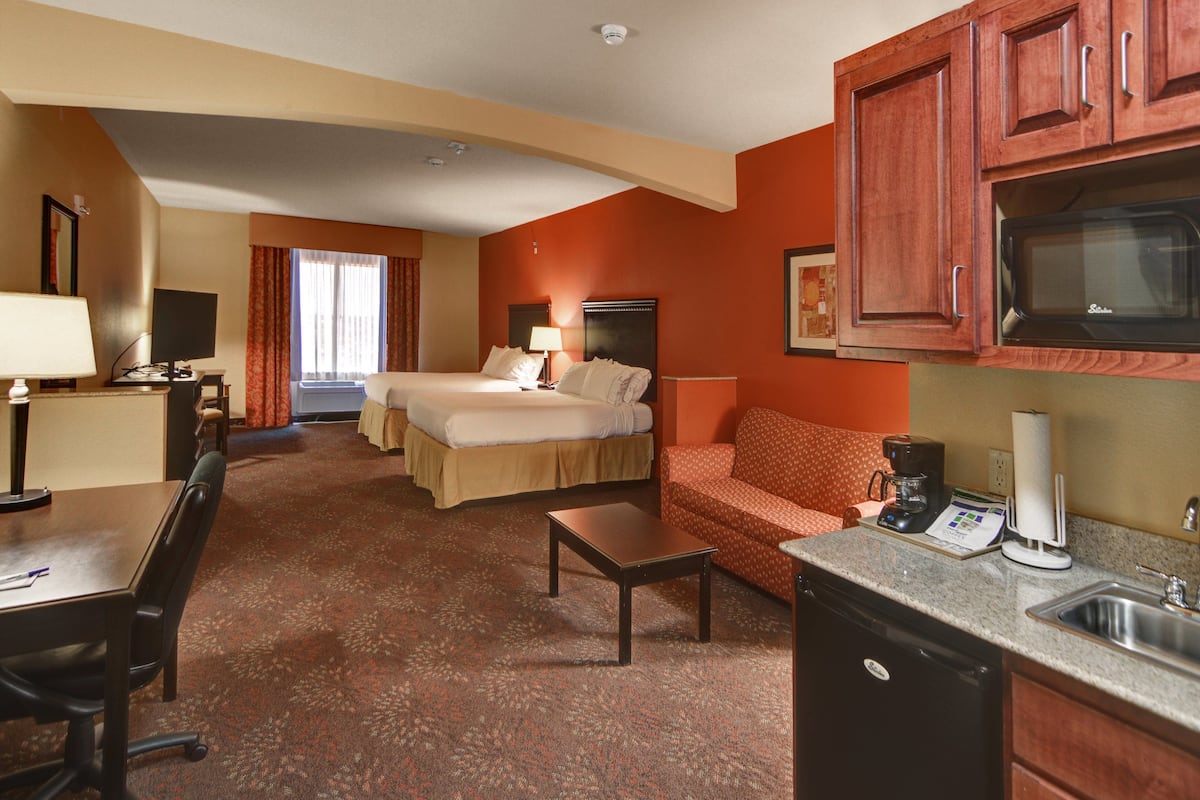 Habitación de hotel con cama, escritorio, cafetera, microondas y lavabo.