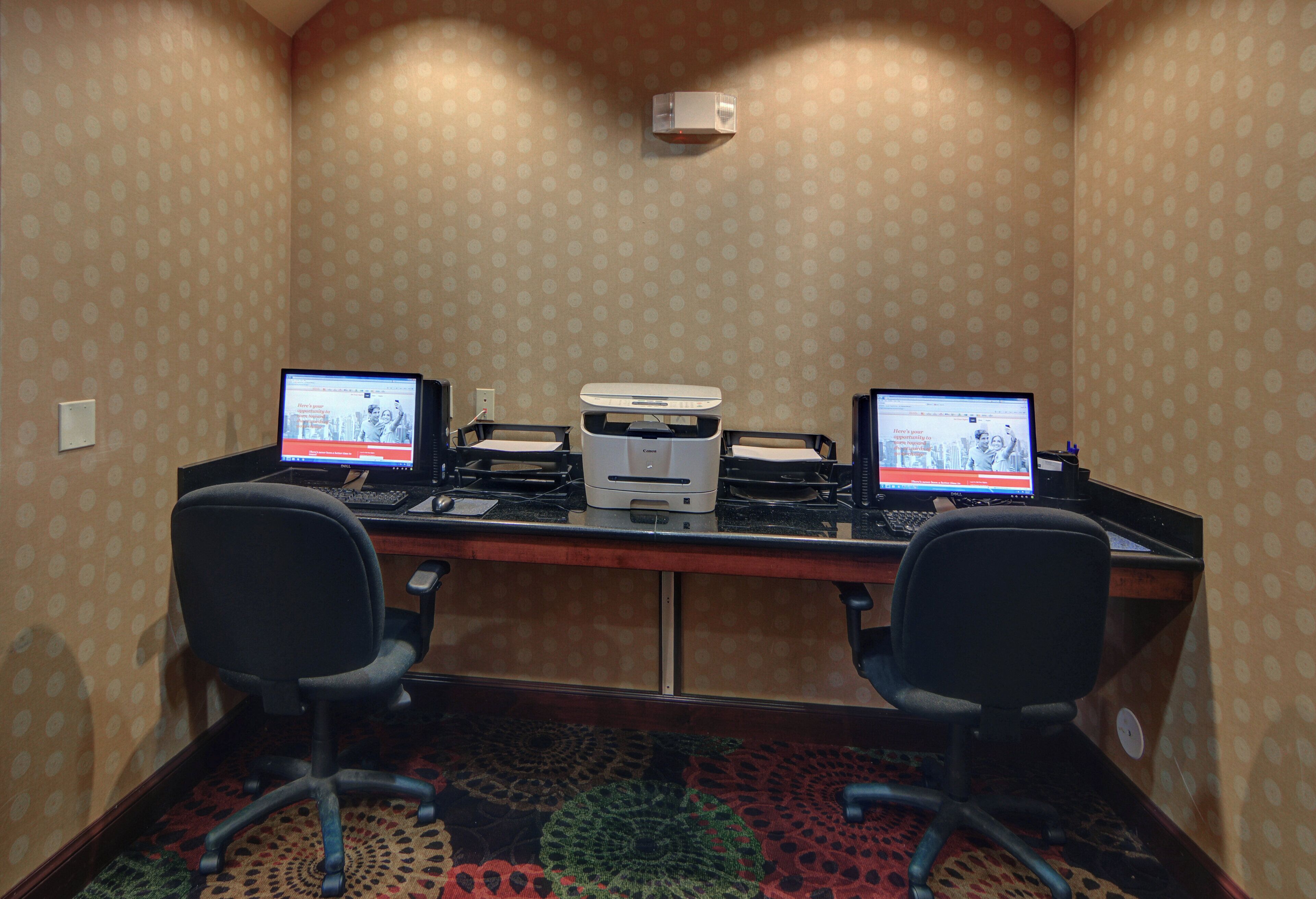A conference room with two desks, each with a computer and a printer.