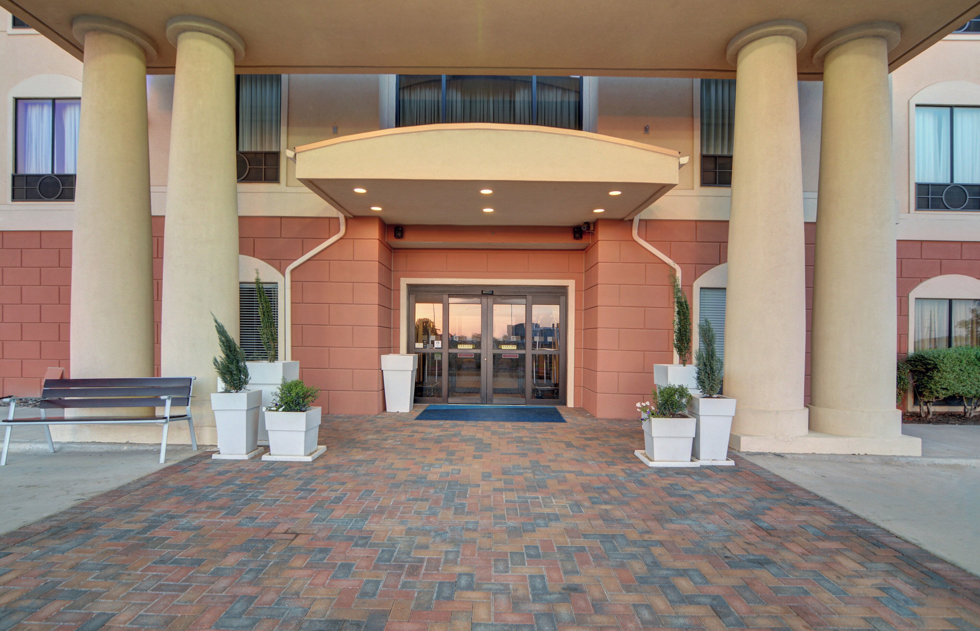 A hotel entrance with a brick-patterned walkway, a covered entrance area, and columns.
