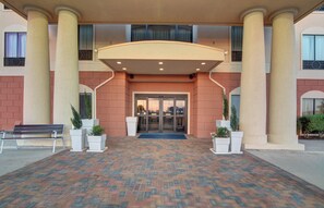 A hotel entrance with a brick-patterned walkway, a covered entrance area, and columns. - Holiday Inn Express & Suites Altus by IHG (Altus)