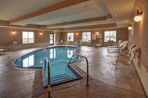 An indoor swimming pool with a tiled floor, a pool ladder, and several lounge chairs around the perimeter.