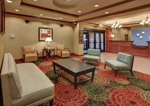 A hotel lobby with a reception desk, seating area with chairs, a coffee table, and patterned carpet.