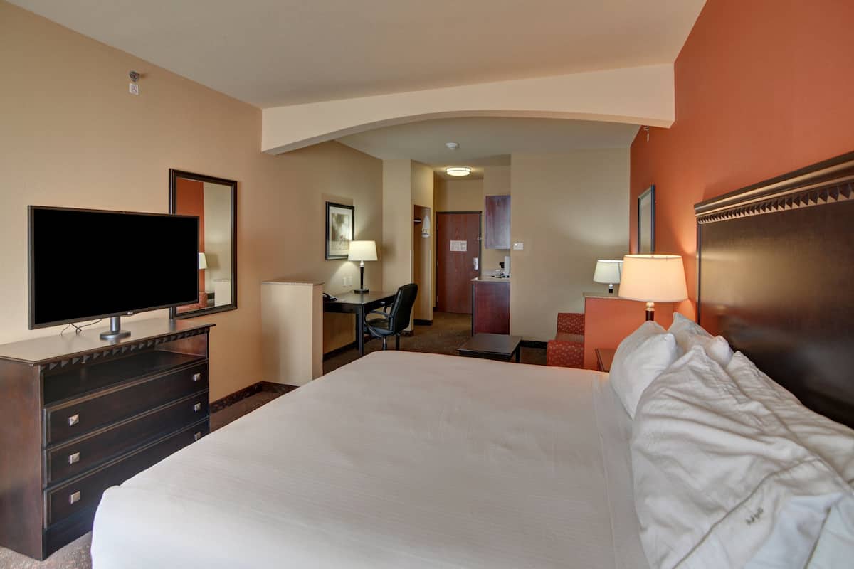 Habitación de hotel con una cama grande, televisor, escritorio con silla, y un baño visible a través de un arco.