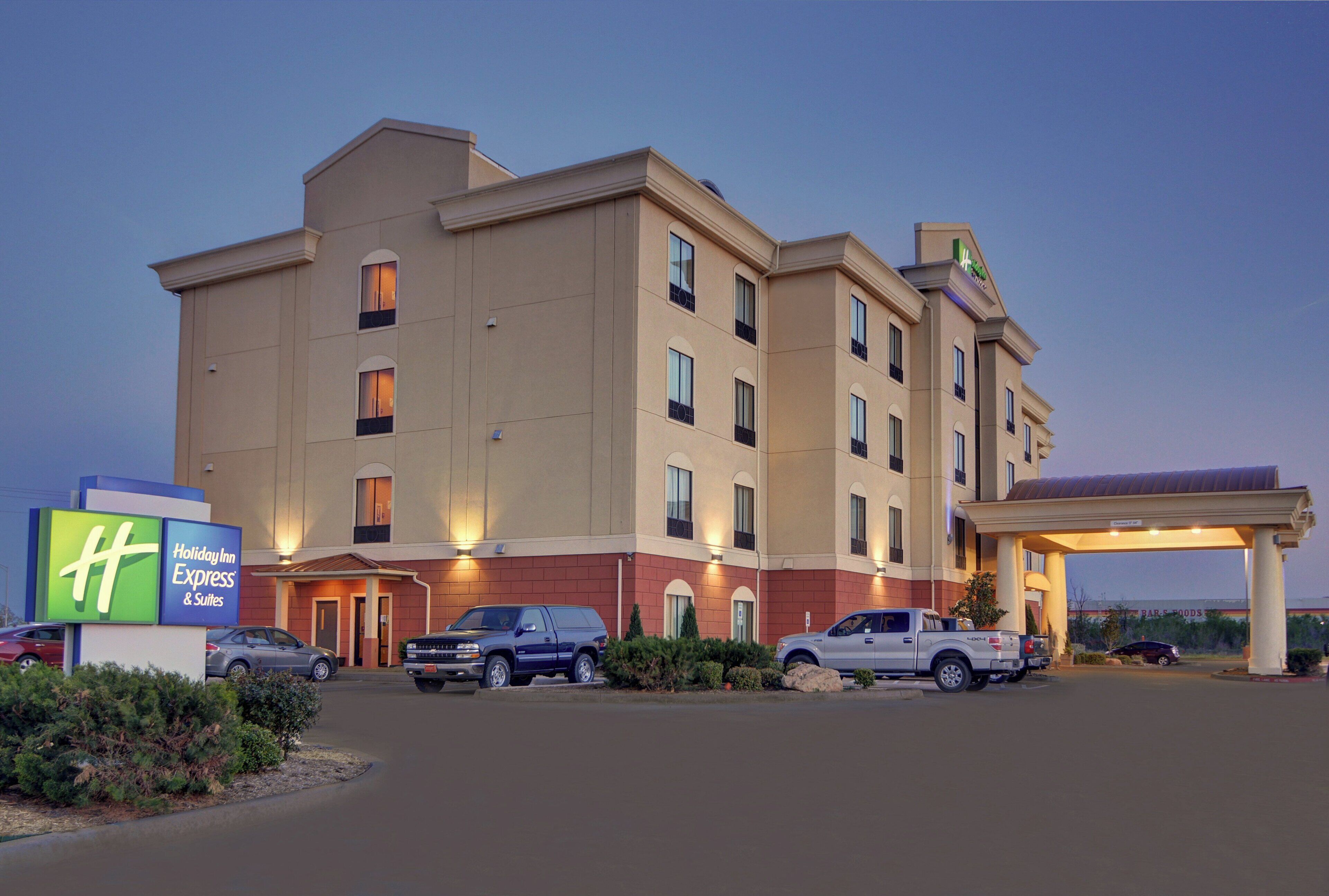 Un hotel Holiday Inn Express con estacionamiento, varios vehículos y una entrada bien iluminada.