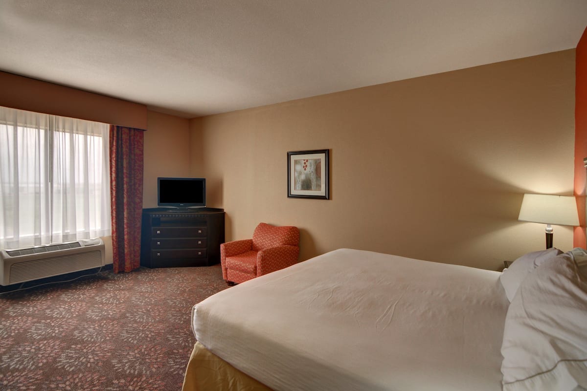 Una habitación de hotel con una cama, un aparador, un televisor, una silla y un cuadro en la pared.