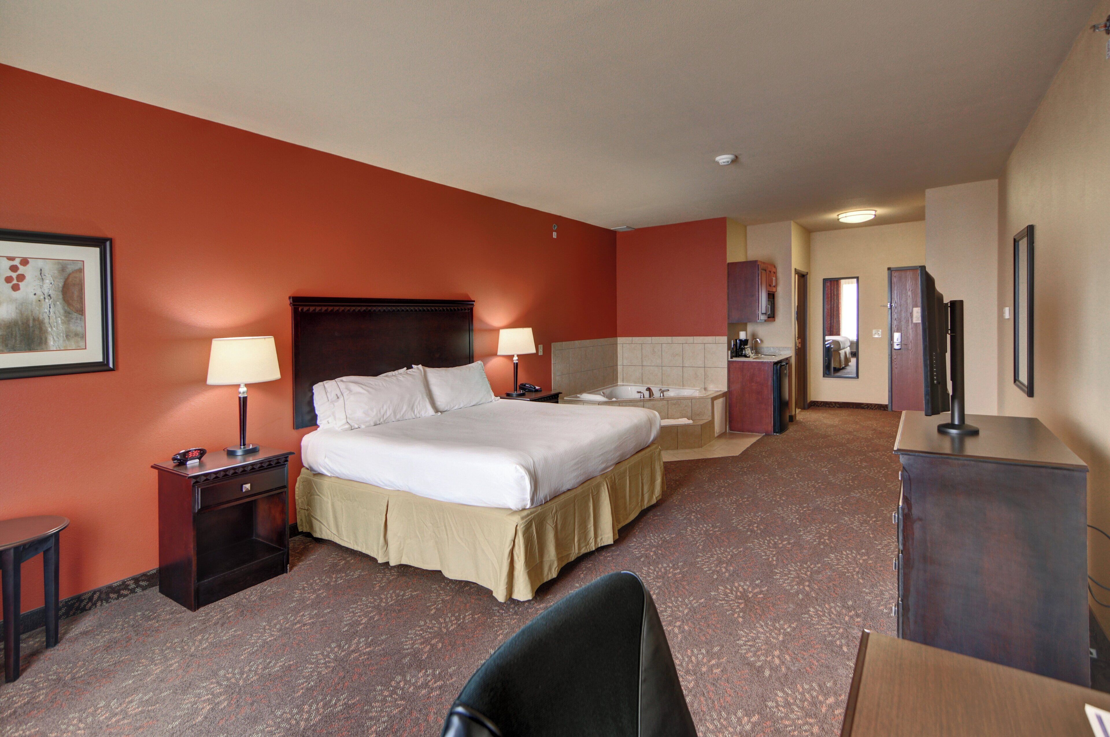 Een hotelkamer met een groot bed, bedlampen, een bureau, een stoel, een televisie en een badkamer met een bad.