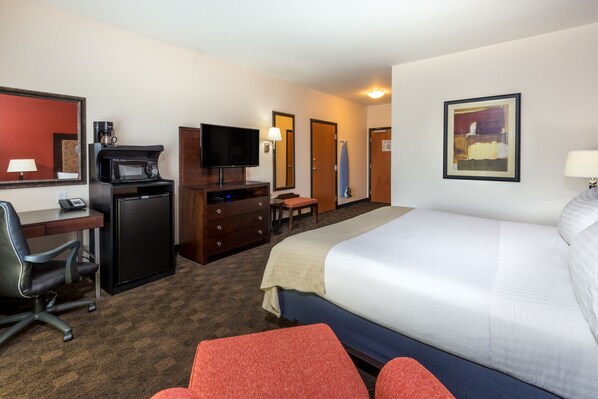 A hotel room with a bed, desk, chair, television, microwave, and a painting on the wall.