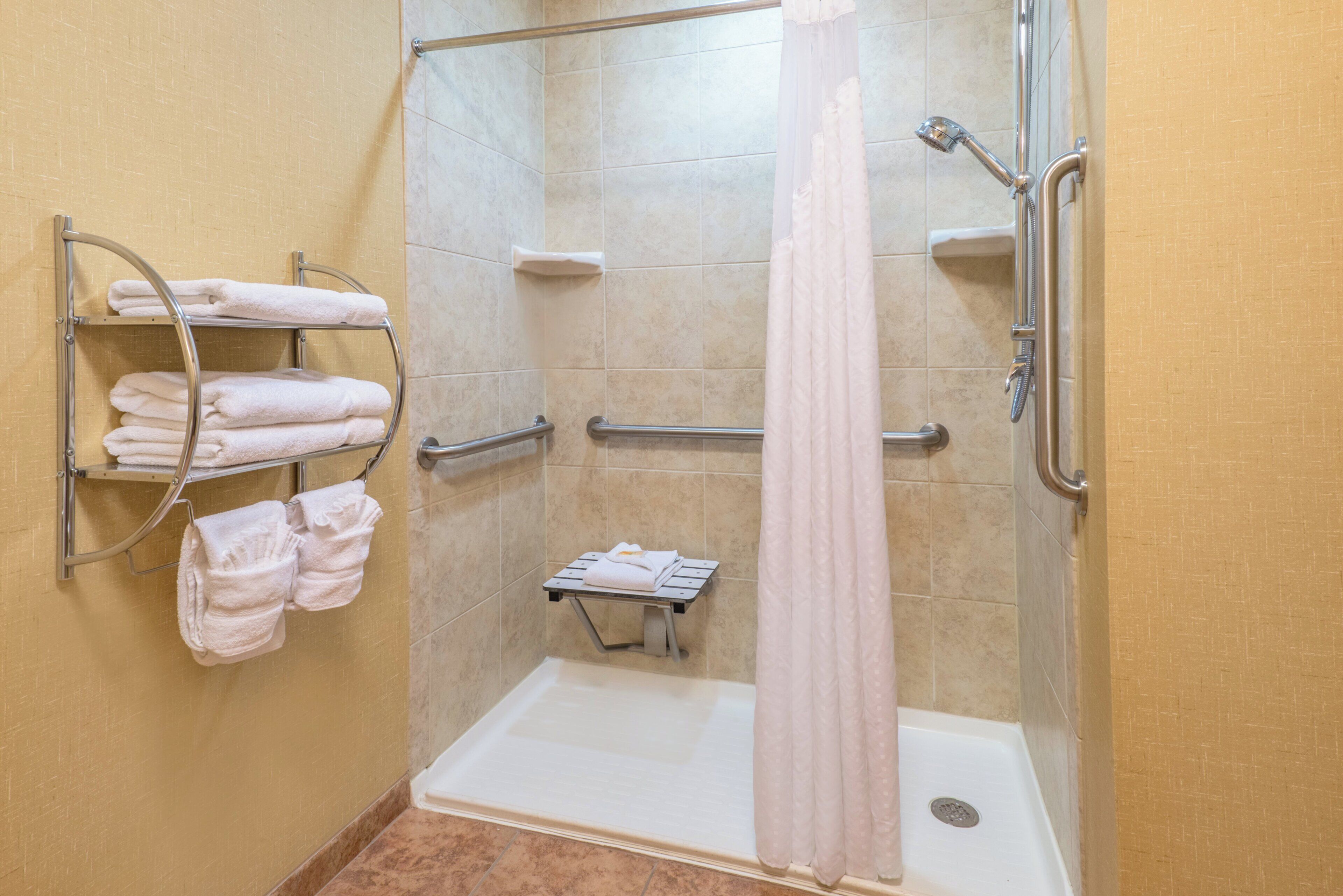 Zona de ducha con puerta de vidrio, un perchero con toallas dobladas, un panel de control de la ducha y una cortina de baño.