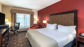 Une chambre d’hôtel avec un grand lit, deux chaises, un bureau, une télévision et une fenêtre avec des rideaux.