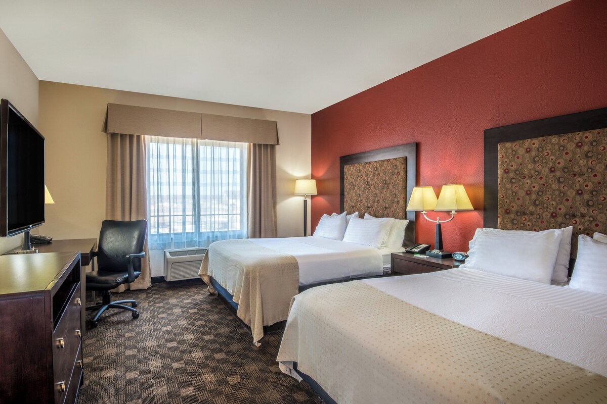 Une chambre d’hôtel avec deux lits, un bureau, une chaise et une télévision.