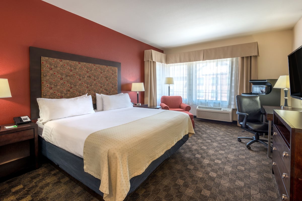 Quarto de hotel com uma cama grande, duas mesas de cabeceira, uma escrivaninha com cadeira, televisão e janela com cortinas.