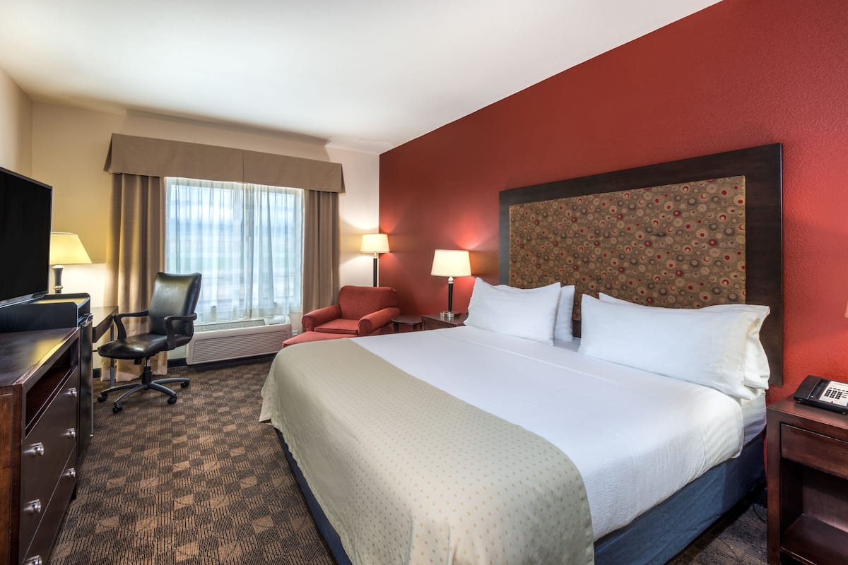 Quarto de hotel com uma cama grande, uma escrivaninha com computador, uma cadeira, duas luminárias e uma televisão.