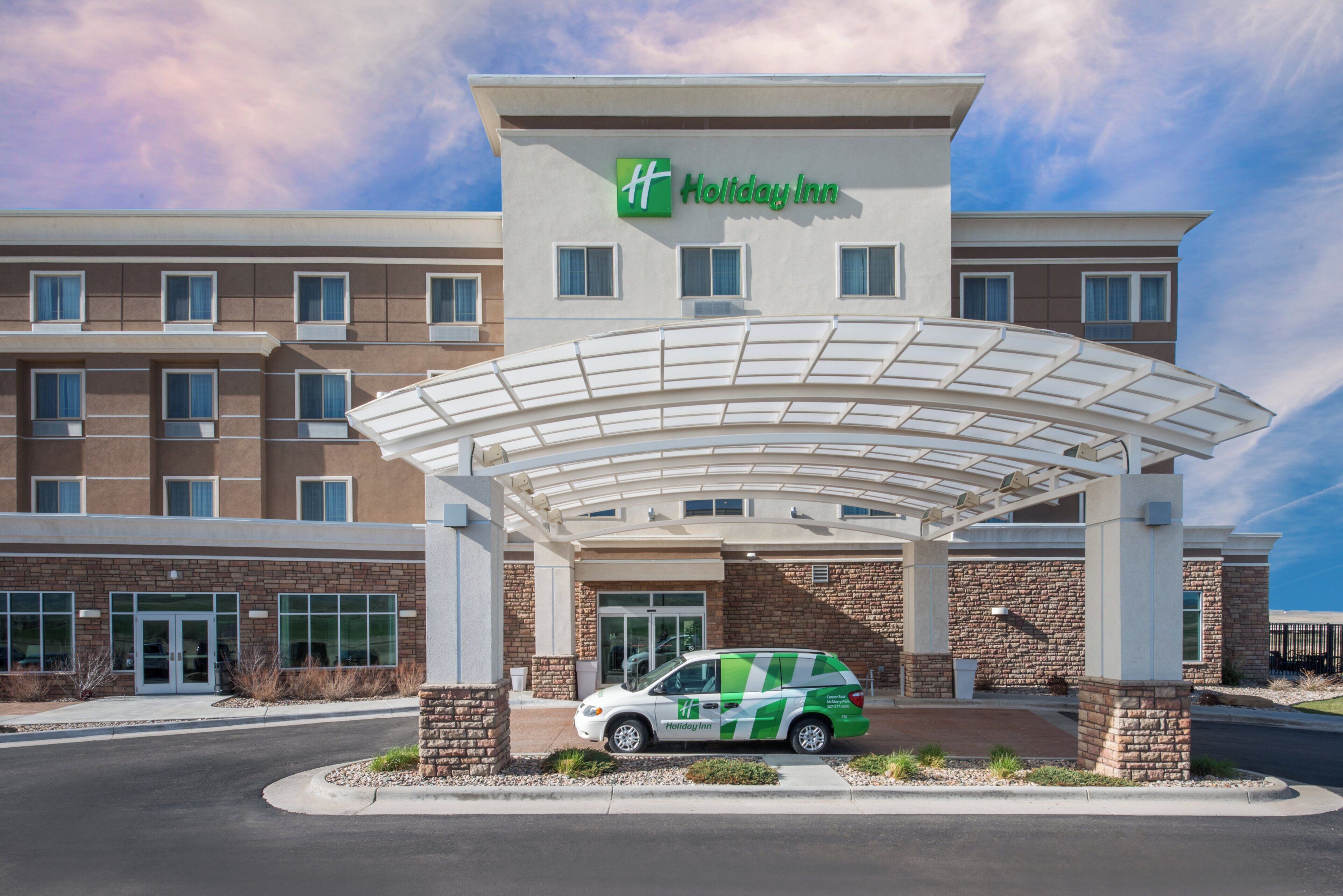 Un hotel Holiday Inn con entrada techada, zona de estacionamiento y servicio de transporte lanzadera verde.