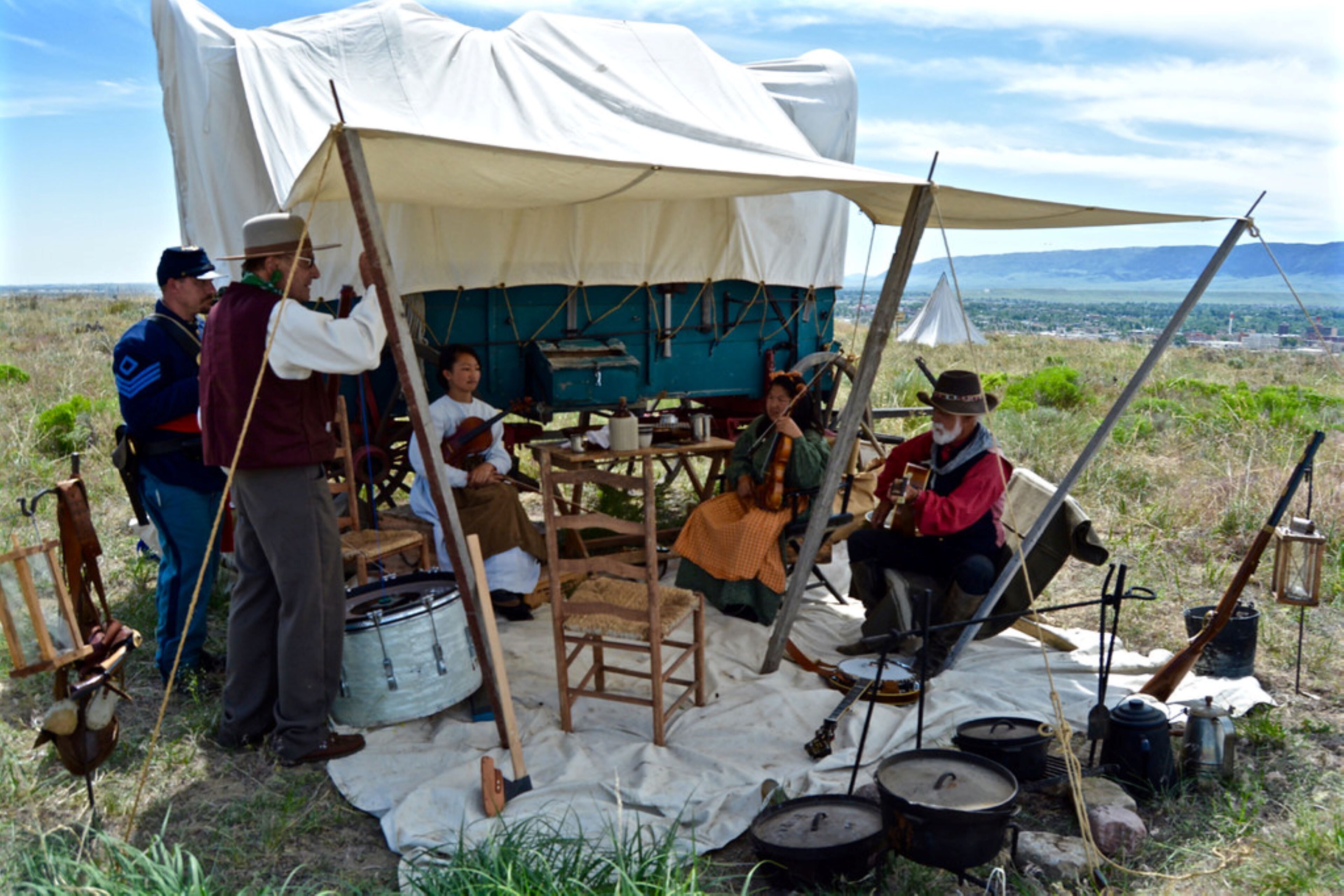 A group of people gathered around a campfire with tents and cooking equipment.