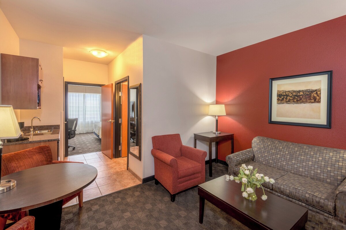 Une chambre d’hôtel avec une table à manger, un canapé, une chaise, une lampe et un tableau encadré au mur.