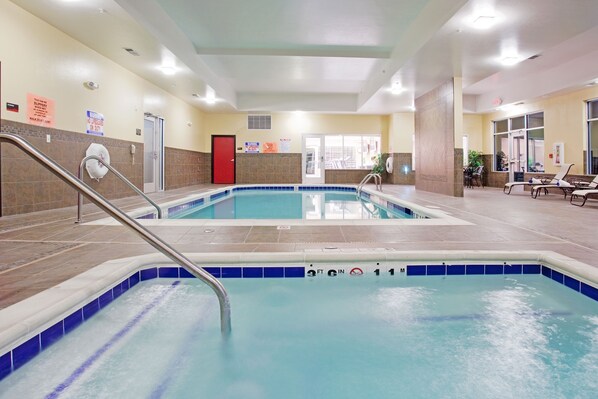 Une piscine intérieure à l’eau claire, avec une porte rouge et un sol carrelé.