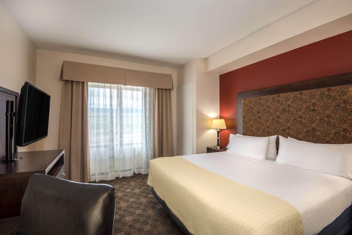 Quarto de hotel com uma cama grande, televisão, escrivaninha e janela com cortinas.