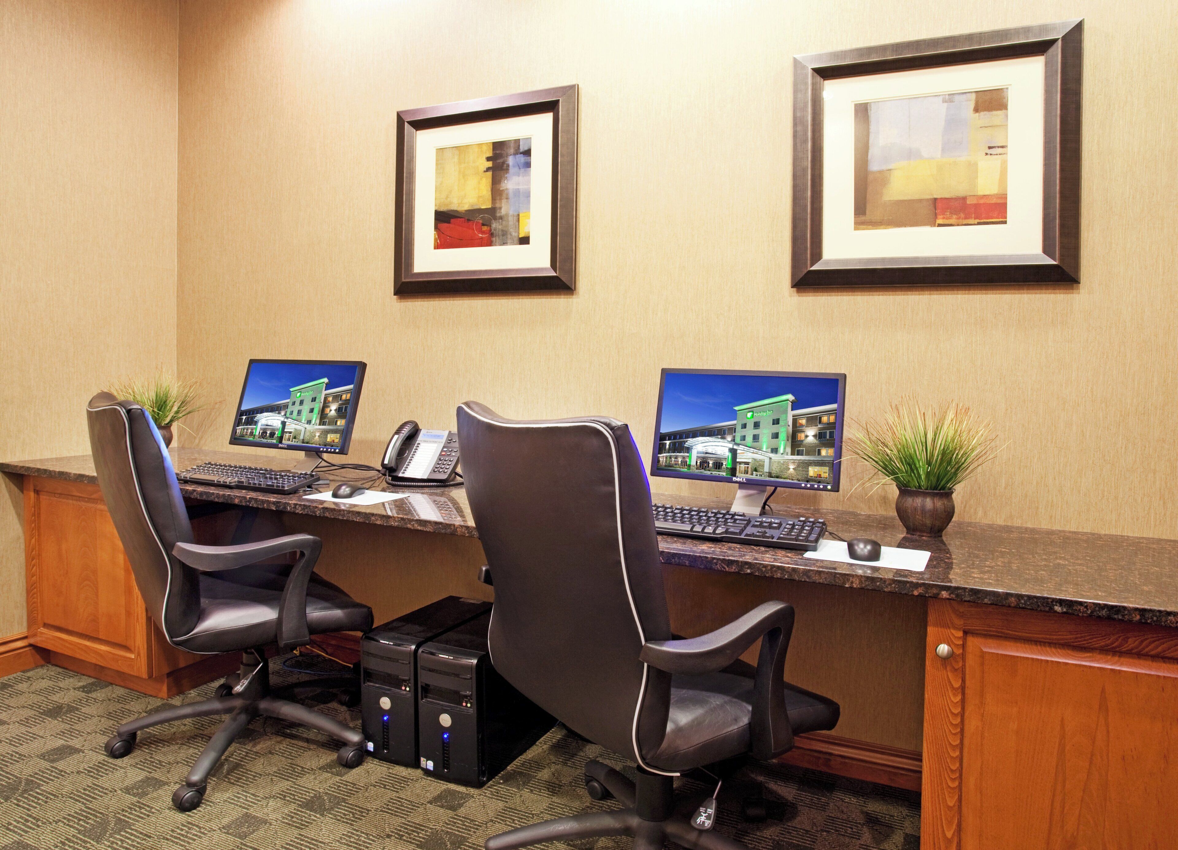 A hotel reception desk with two computer monitors, a telephone, and two chairs.