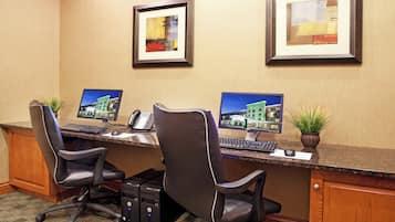 A hotel reception desk with two computer monitors, a telephone, and two chairs.