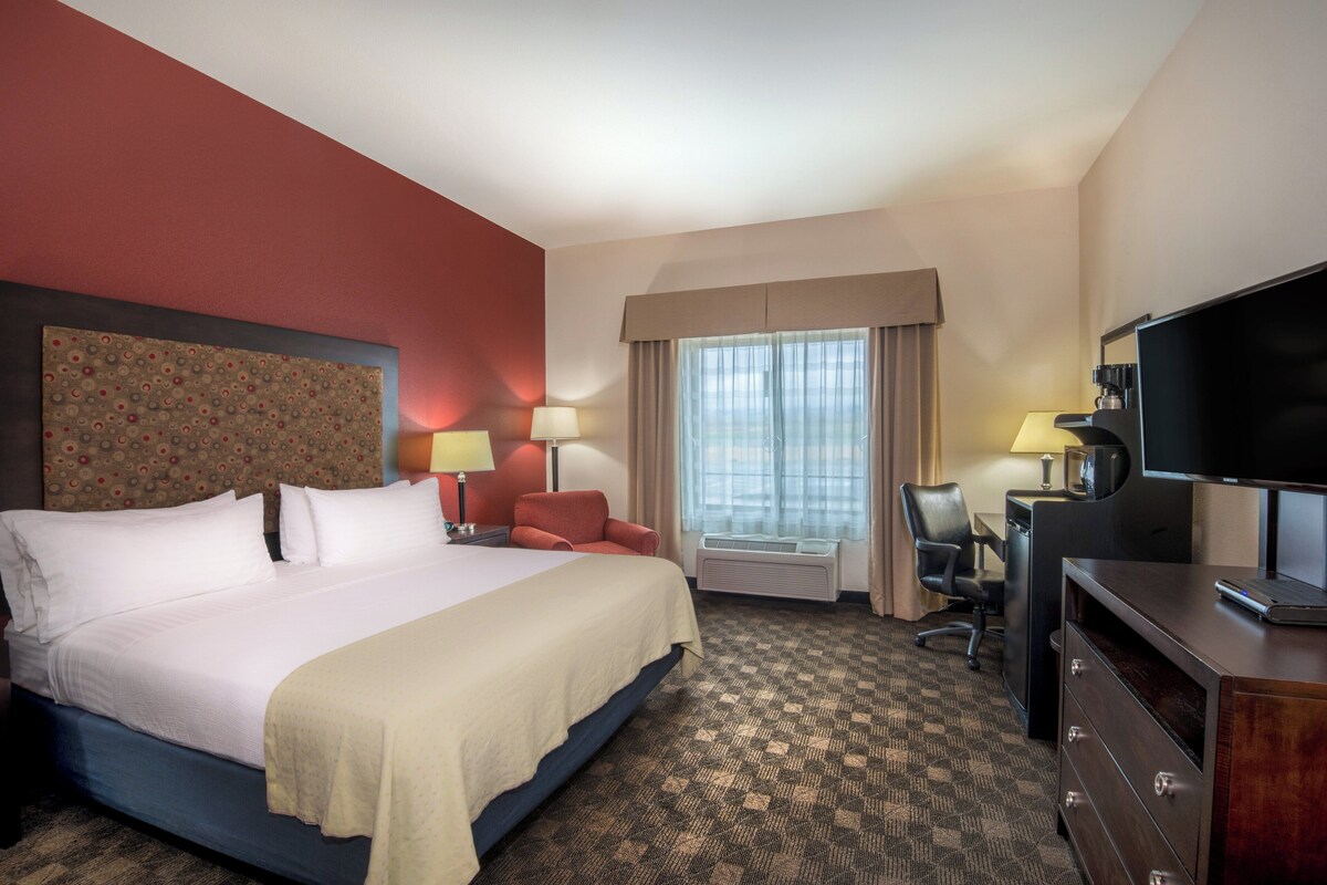 Une chambre d’hôtel avec un grand lit, un bureau avec un ordinateur, une télévision et une fenêtre avec des rideaux.