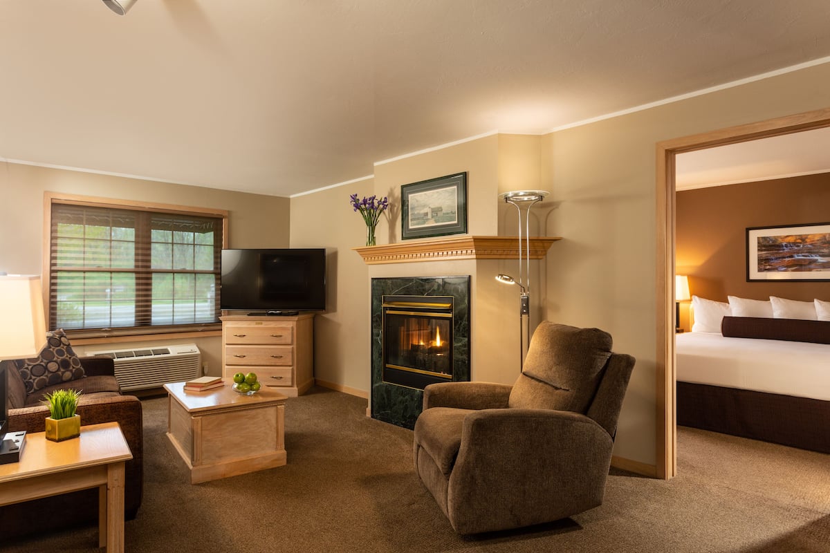 A hotel room with a fireplace, a television, a sofa, a desk, and a bed.
