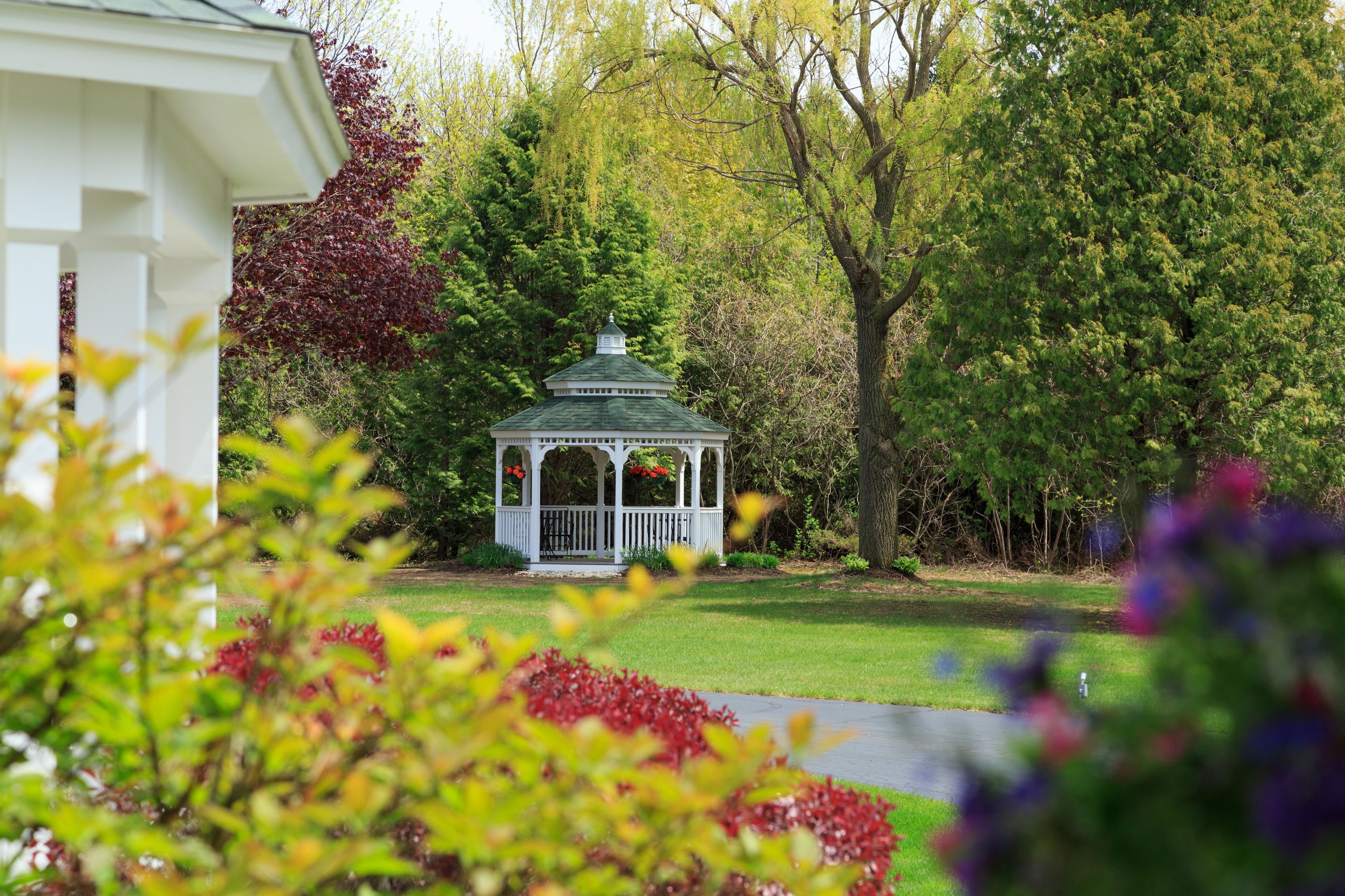A gazebo with a green roof and white railing, surrounded by lush greenery and trees.