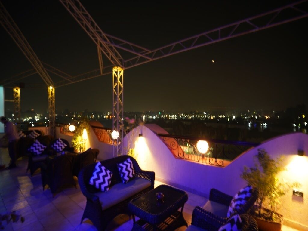 Un espacio al aire libre con sillas y mesas, una barandilla y vistas de la ciudad de noche.