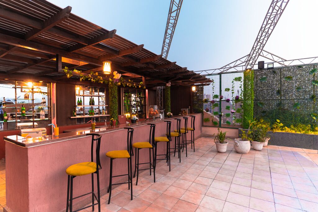 A rooftop bar with a wooden pergola, bar stools, and potted plants.