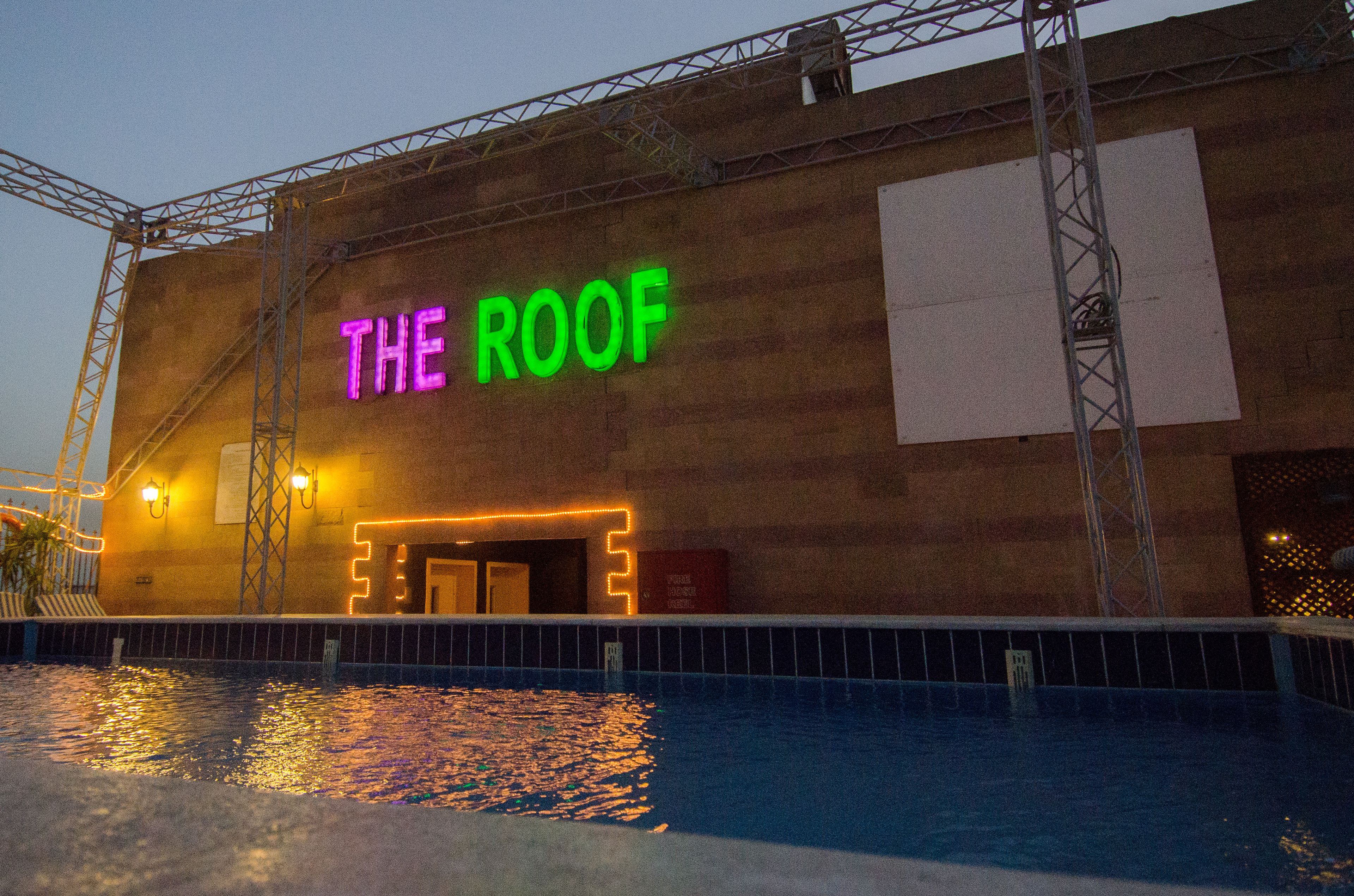Un bâtiment avec une enseigne au néon indiquant « THE ROOF » et une piscine devant.