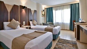 A hotel room with two beds, a desk, a chair, and a view of the outdoors. - Swiss Inn Nile Hotel (Giza)