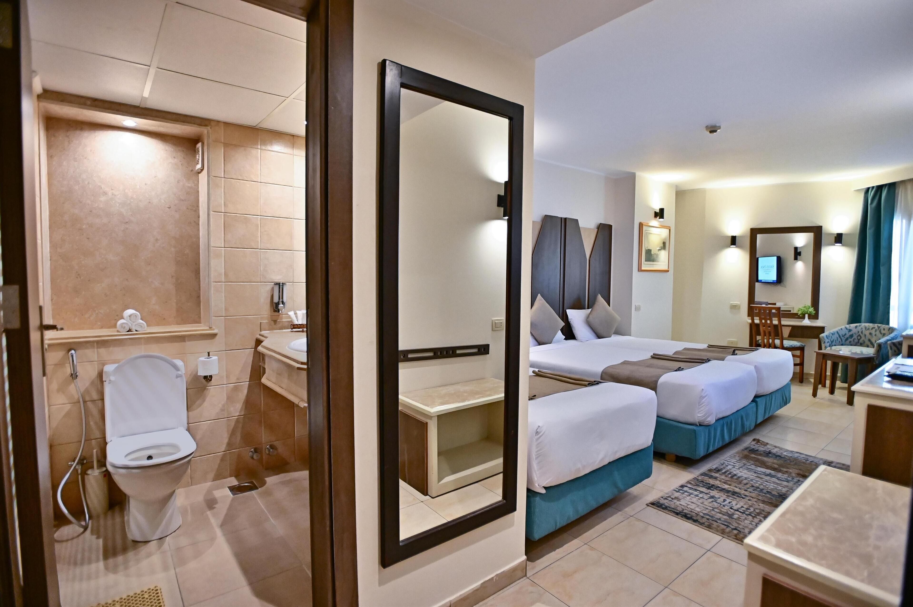 A hotel room with a bathroom, a bed with two pillows, a desk, and a chair.