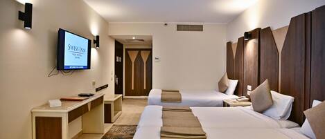 A hotel room with two beds, a desk, and a TV displaying the hotel name.