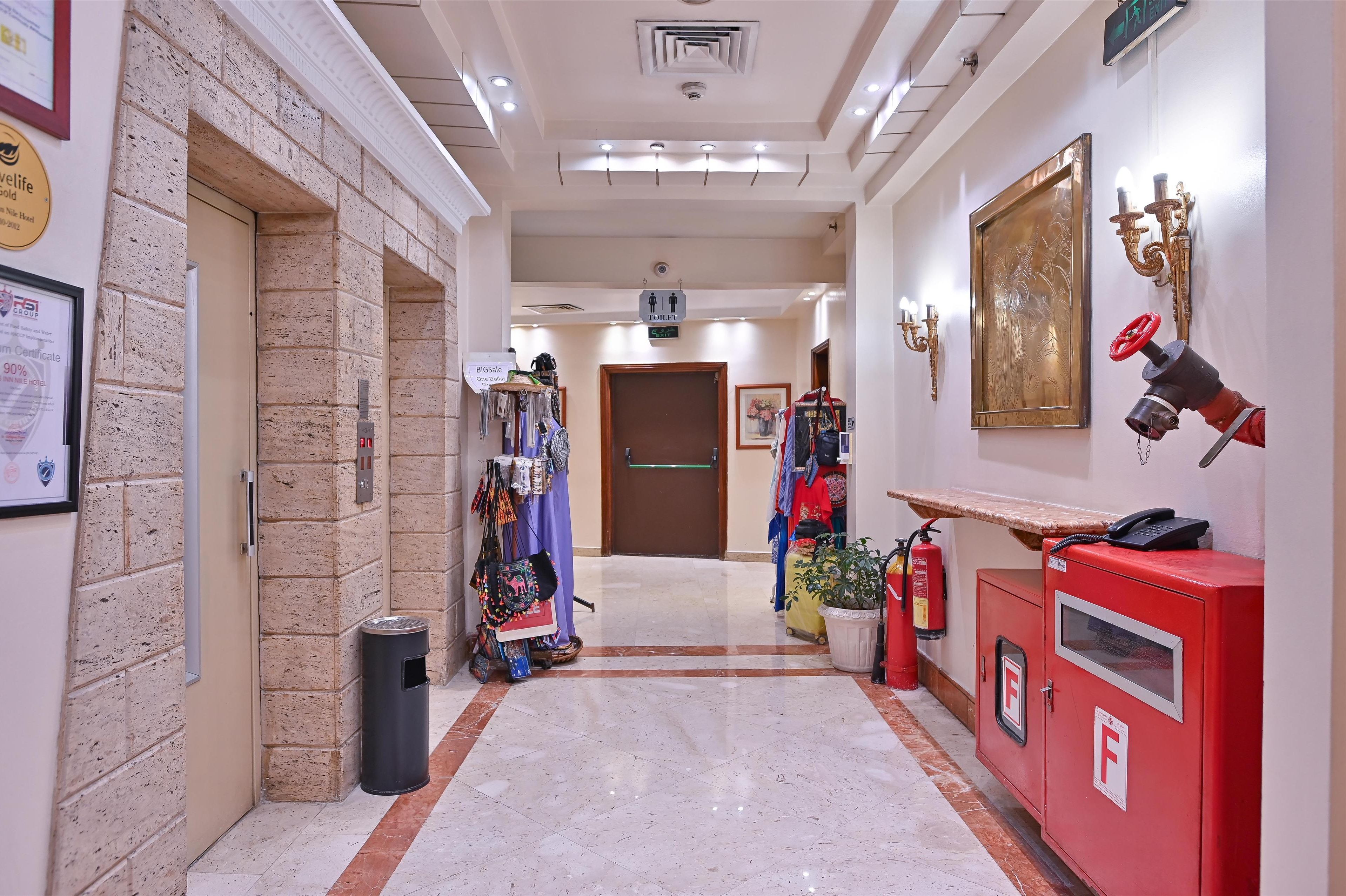 A hotel corridor with a fire extinguisher, a red phone, and a fire hose on the right.