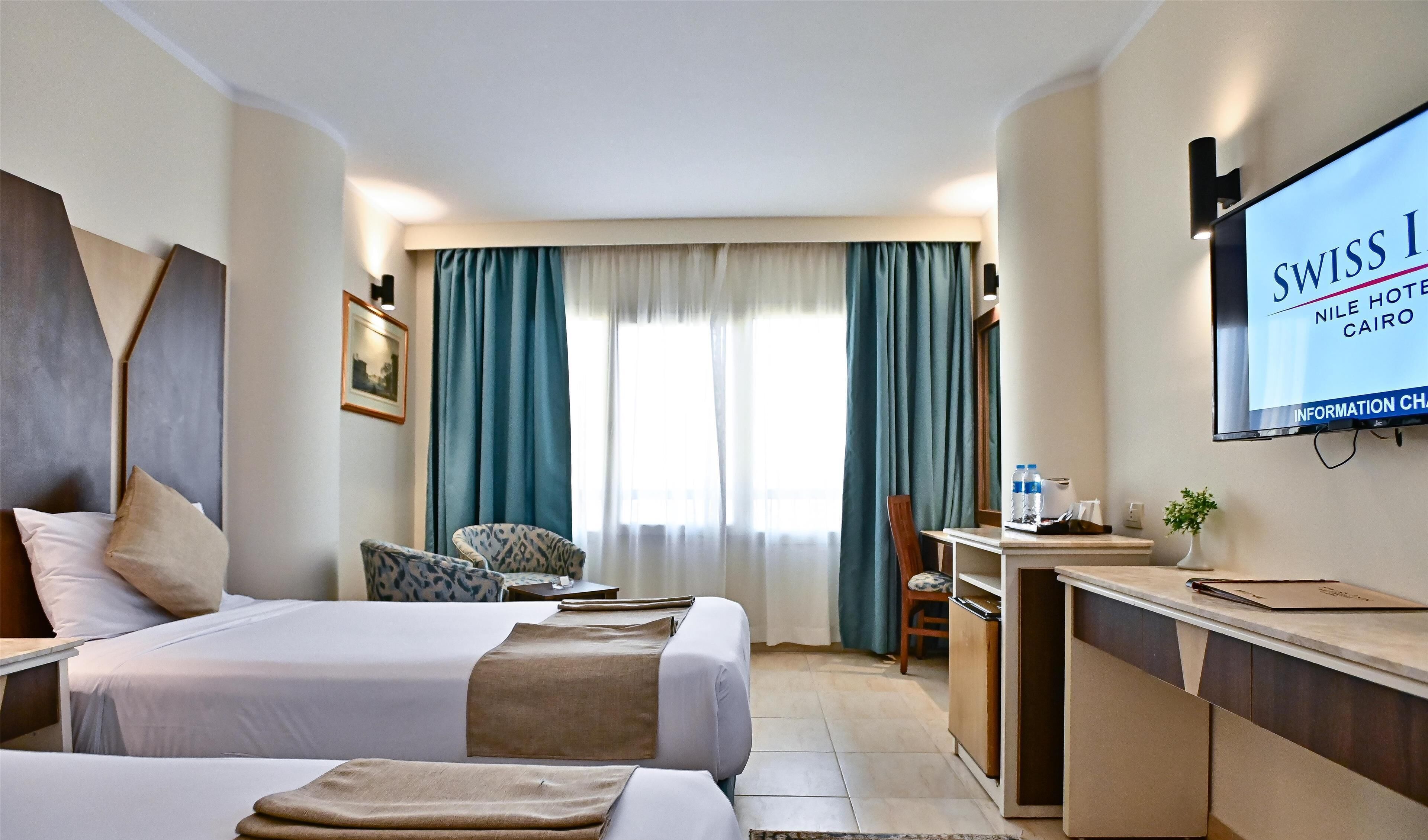 Une chambre d’hôtel avec deux lits, un bureau, une chaise, une télévision et une fenêtre avec des rideaux.