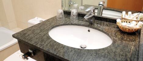 Un baño con encimera de granito, un lavabo blanco, un espejo, un inodoro y una cesta de artículos de aseo.