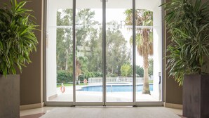Una habitación con un gran ventanal corredera que da a una zona de piscina, rodeada de plantas en macetas.