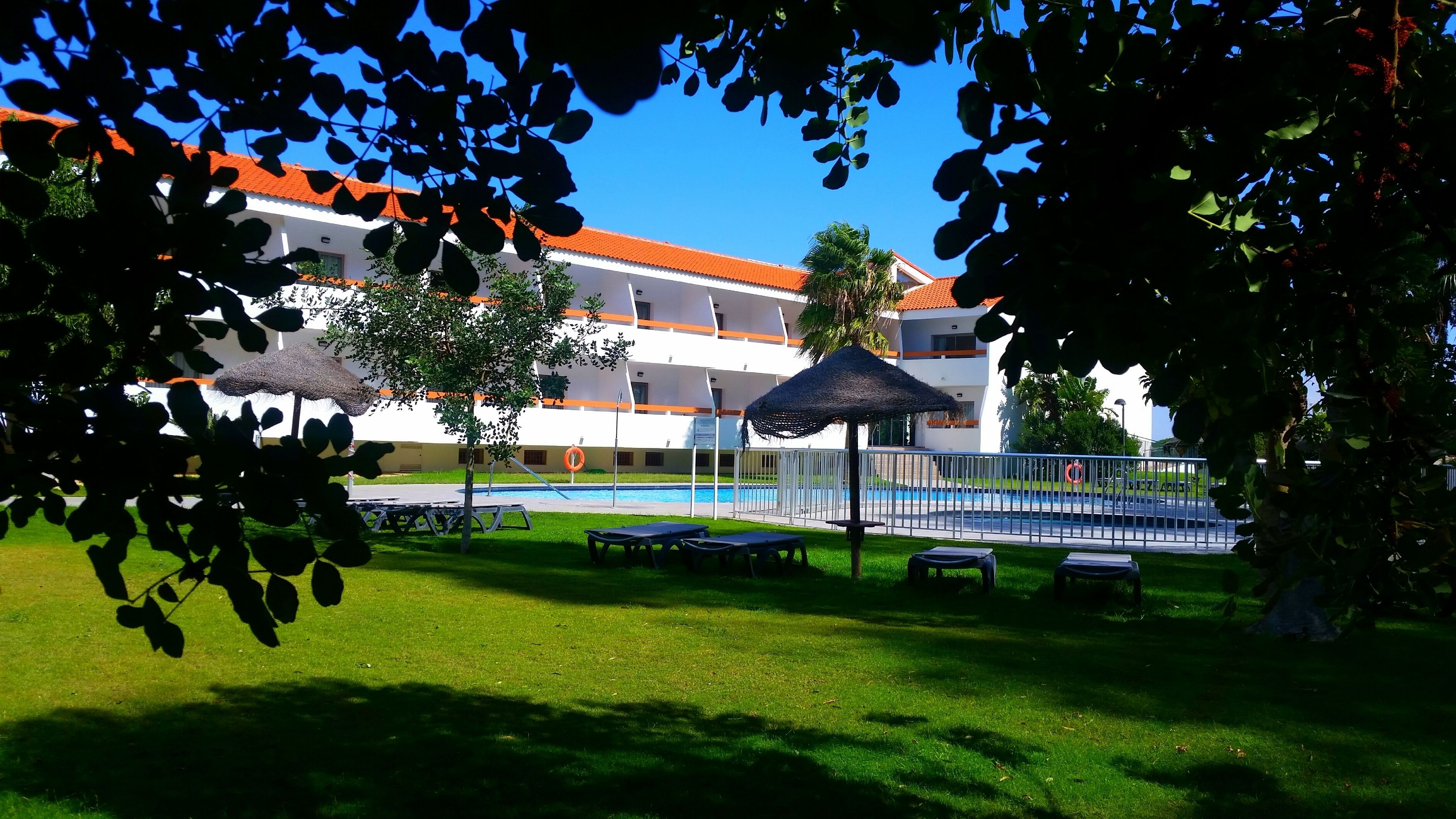 A hotel with a swimming pool, outdoor seating, and a thatched umbrella.