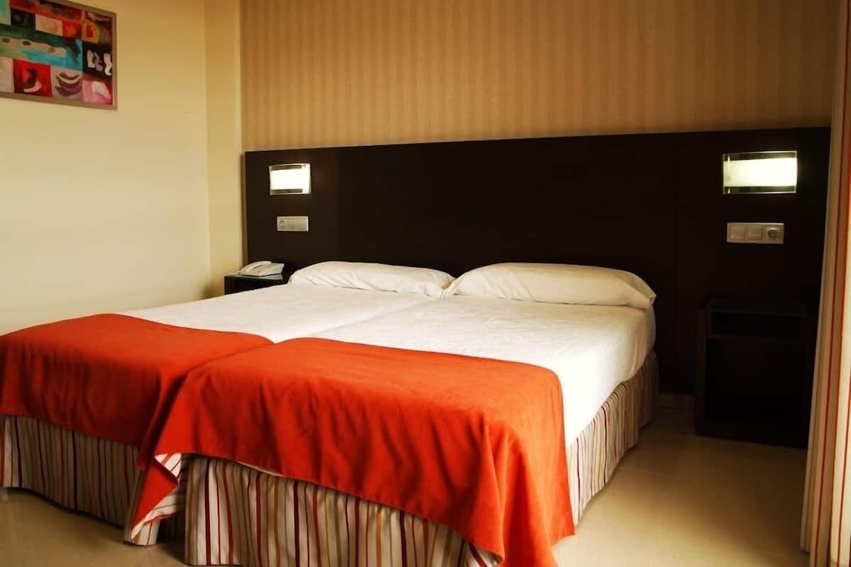 Quarto de hotel com uma cama grande, duas mesas de cabeceira e um telefone fixado na parede.