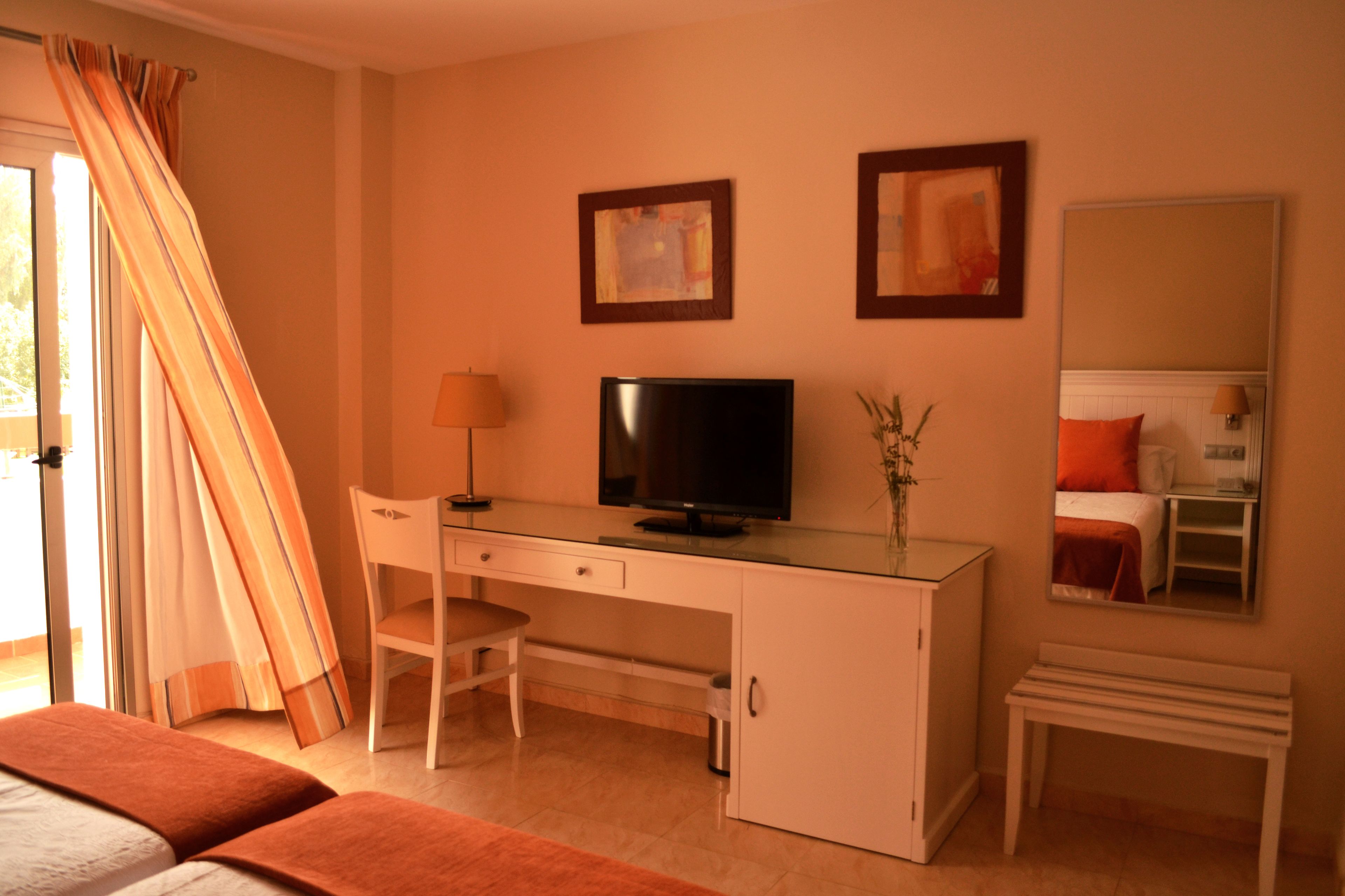 Habitación de hotel con escritorio, silla, televisor, cama y espejo.