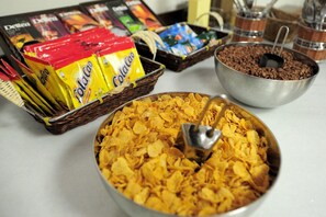 Una mesa de buffet con diferentes alimentos, como cereales, chocolate y aperitivos.